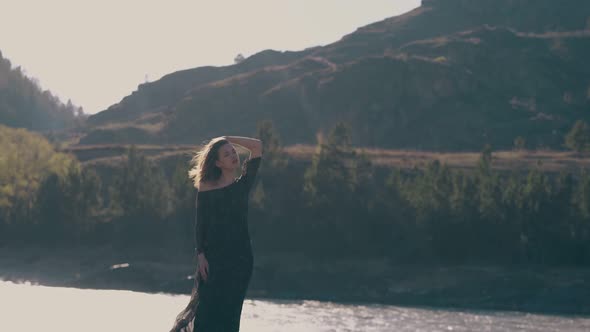 Pretty Girl in Stylish Dress Stands Against Mountain River