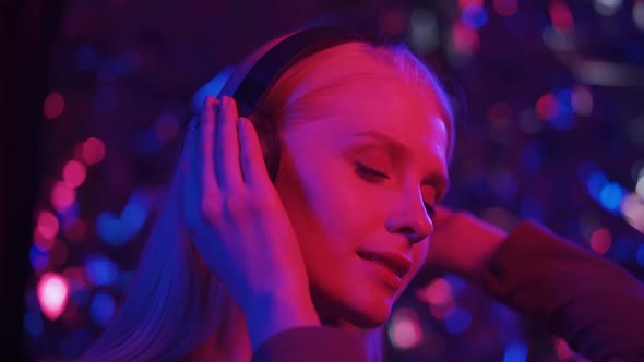 Stylish Woman Listening Music in Headphones and Dancing Energetic and Rhythm in Pink and Blue Light