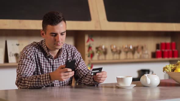 Handsome Man Making Purchase Online, Typing Credit Card Details on Black Smartphone in the Modern