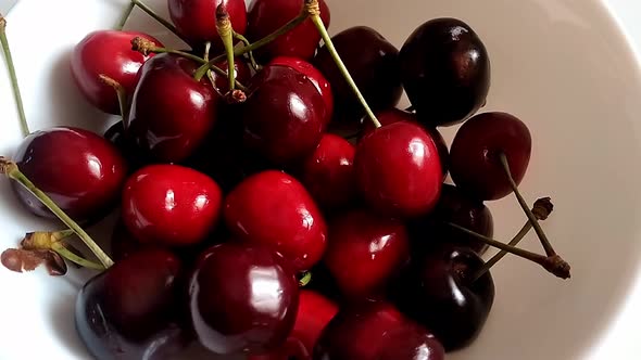 Close up of a bunch of cherries on a white ceramic bowl. Some still have their tails. They are ripe