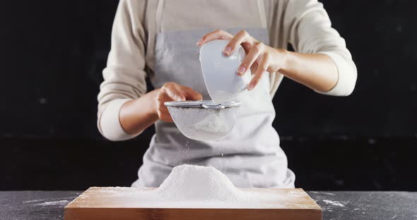 Woman sieving flour from the bowl on the wooden board 4k