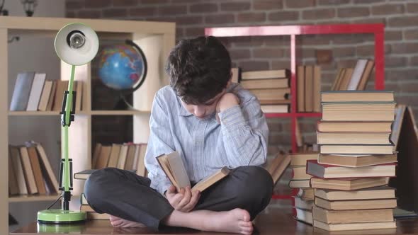 Reading of books. schoolboy sits cross-legged on Desk and reads open textbook