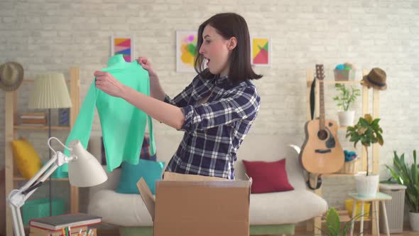 Young Woman Happily Opens a Box with a Parcel
