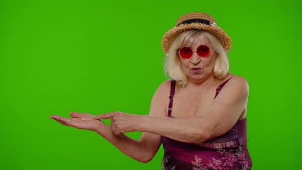 Senior Old Woman Tourist in Swimsuit Points Fingers on Left at Blank Space Shows Advertising Content