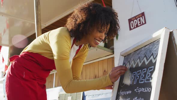 African american woman wearing apron writing on food menu slate board of the food truck