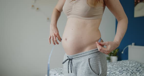 Young Pregnant Woman Measures Abdominal Circumference with a Measuring Tape