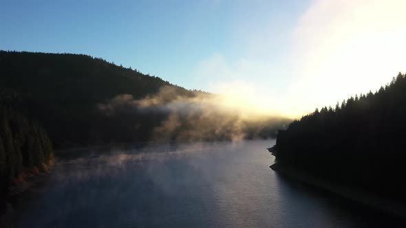 Aerial View of a Misty Lake. Dawn Dark Lights During Sunrise, Cold Weather. Flying Over Clouds