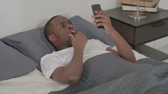 African Man Reacting to Loss on Smartphone in Bed