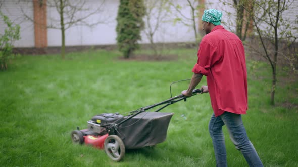 African American Young Man Walking with Lawnmower at Backyard