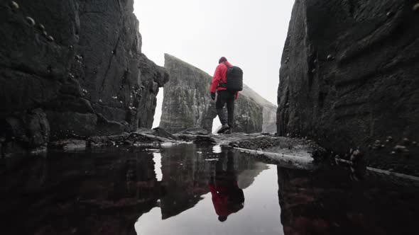 Man in Red Jacket Walking By Rocky and Shallow Rocks in Faroe Islands