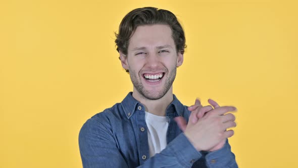 Positive Young Man Clapping and Cheering on Yellow Background