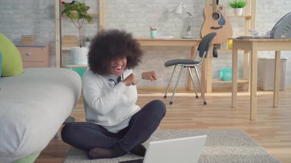 Beautiful African American Woman with an Afro Hairstyle Sitting on the Floor with a Laptop Learned