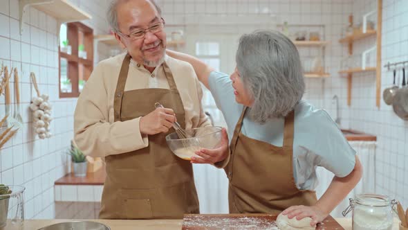 Asian Senior elderly couple stand in kitchen at house enjoy retirement life cooking food together.