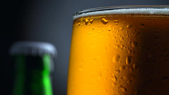 Wet Rotating Mug of Light Beer and a Top of a Green Beer Bottle. Black and Gray Background. FHD