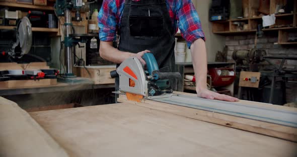 The Master Cuts a Wooden Board with a Circular Saw in the Woodworking Workshop of a Small Furniture