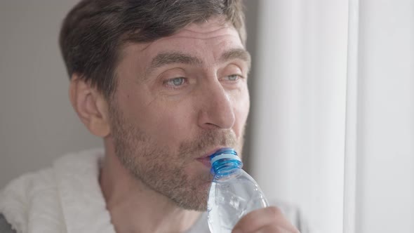 Headshot Portrait of Perspiring Man Wiping Forehead with Hand Drinking Refreshing Water From Bottle