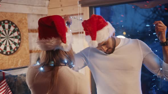 Happy Young Couple Dancing with Christmas Lights and Santa Hats