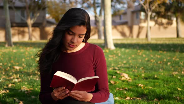 A young woman school girl studying and reading a book on a campus lawn or outdoor park SLOW MOTION.