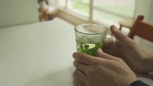 Man holding a glass of hot mint tea on a table in cozy apartment with garden