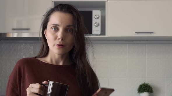 Attractive Young Woman Smiling Playing Hair Beautifully Dances with a Mug of Coffee and a Phone in