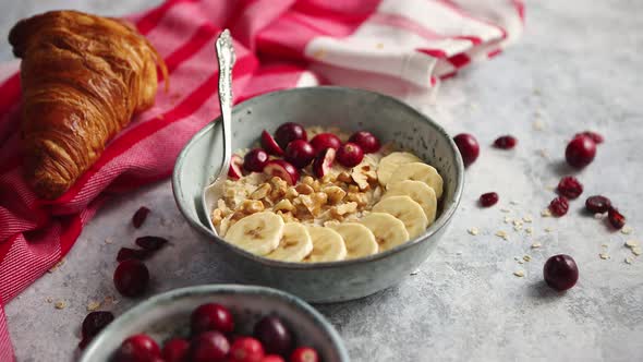 Ceramic Bowl of Oatmeal Porridge with Banana, Fresh Cranberries and Walnuts