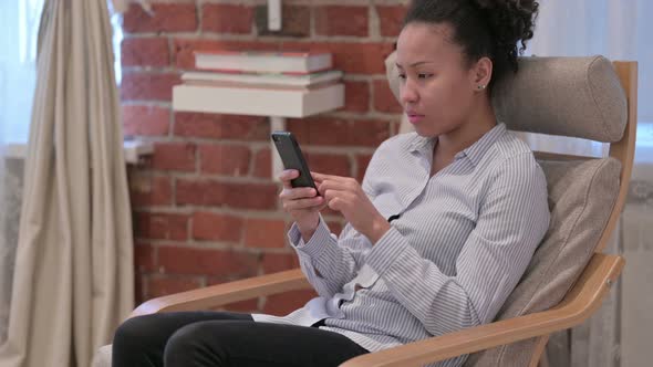 African Woman Reacting to Loss on Smartphone at Home