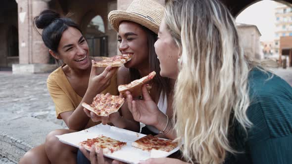 Three Cheerful Multiracial Women Eating Pizza in the Street