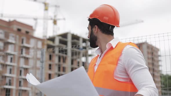 Construction Engineer Holding a Project in His Hand. He Checks a Drawing on the Construction Site