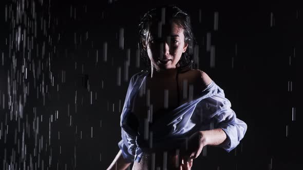 Beautiful girl in a black swimsuit and shirt stands in the rain, enjoying the drops of water. Flying