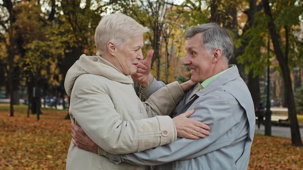 Joyful Middle Aged Elderly Couple Hugging Laughing Standing in Autumn Park Carefree Chatting Happy