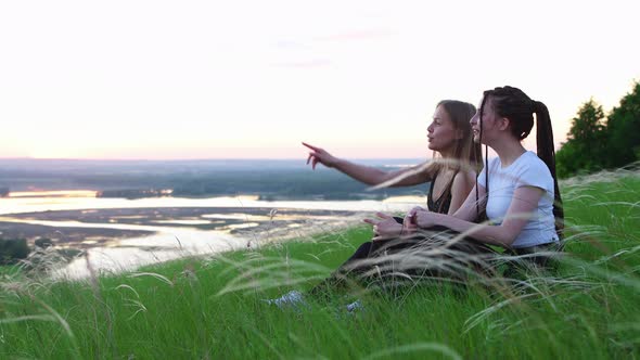 Two Young Women Sitting in the Grass and Watching the Sunset  Pointing at the Sky