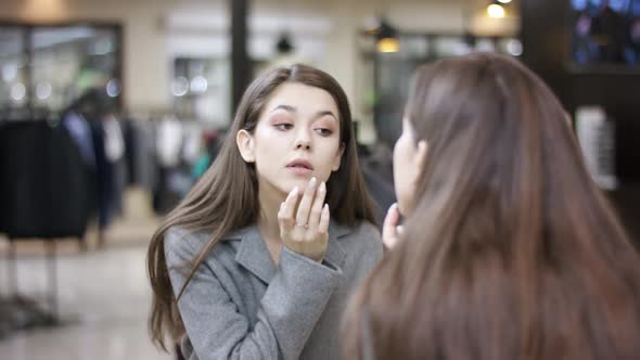 A Close Up View From the Back of a Young Woman in a Grey Overcoat Looking at Herself in the Mirror