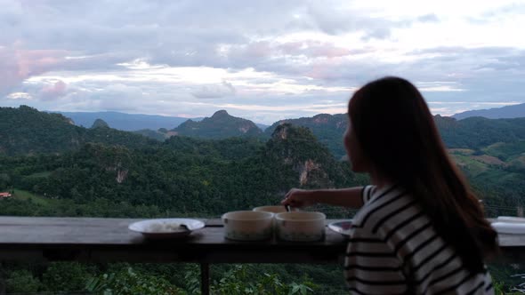 An asian woman eating food while sitting on balcony with greenery mountains view