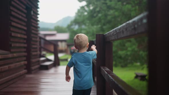Toddler Boy Walks Touching Wooden Railing on Veranda