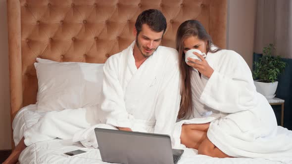 Young Couple Having Coffee in Bed While Using Laptop