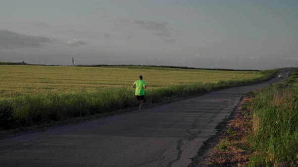 Man in neon green running past camera and wheat fields on spring evening