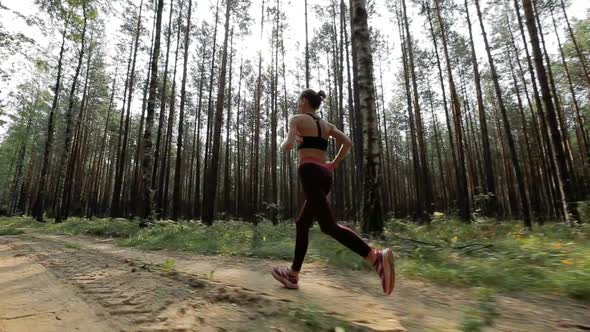 Happy Young Woman Is Jogging in a Forest or in a Park Among Trees. Tracking Shot with Stabilized