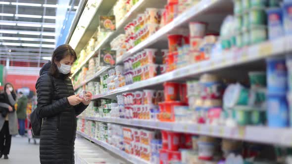 Woman in a Winter Jacket Chooses Dairy Products in the Supermarket