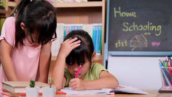 Two cute little sisters learning at home during quarantine. Older sister helping young sister with h alt