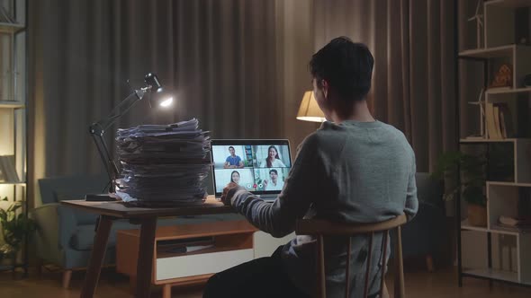 Back View Of Asian Man Having Video Call On Laptop While Working With Documents At Home