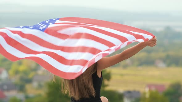 Young Pretty American Woman with Long Hair Holding Waving on Wind USA Flag on Her Sholders Standing