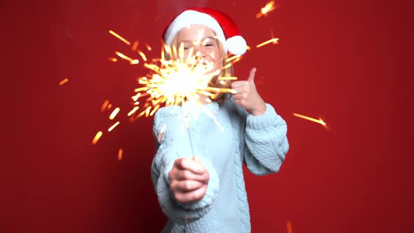 Happy Little Girl in Santa Claus Cap Holding Bengal Light on the Red Background