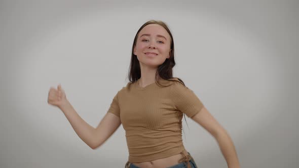 Young Flexible Slim Woman Dancing at Grey Background with Thumbs Up Smiling Looking at Camera