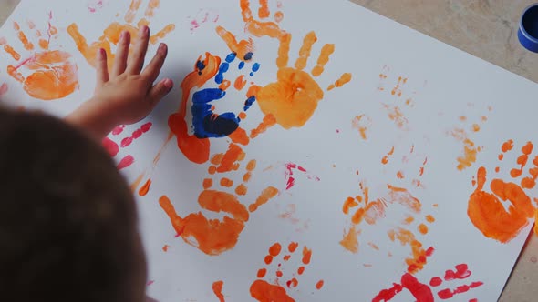 Little Girl with Paints on Her Hands Draws on White Paper