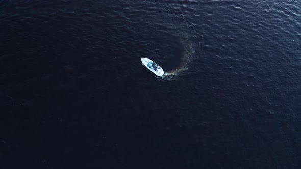 White Small Motor Boat Moves in a Circle and Turns Around with a Trace on the Deep Blue Water