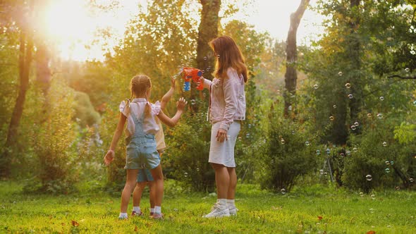 Little Daughters Trying to Catch Soap Bubbles Flying in Air Have Fun with Mom