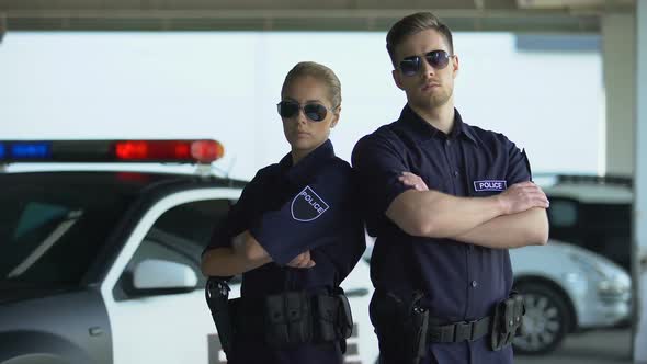 Brave Policewoman and Man in Sunglasses Standing With Folded Hands Near Car