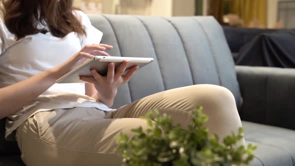 A Girl Touches a Tablet Sitting on the Couch at Home