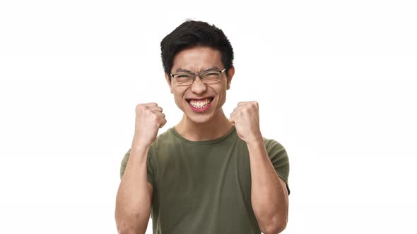 Portrait of Satisfied Asian Man Wearing Glasses and Basic Tshirt Rejoicing with Clenching Fists