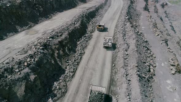 Mining Dump Trucks in Large Granite Open Pit Mine. Loaded Truck Rides on Road Quarry Ledge Drone